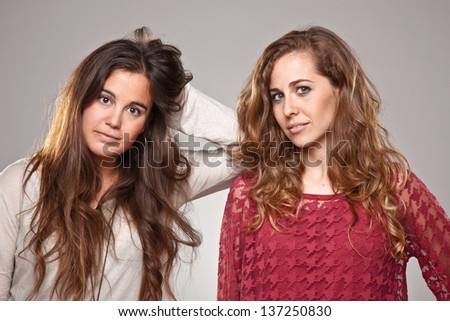 Portrait of two cheerfully young girls looking at the camera. / Studio shot against a grey background.