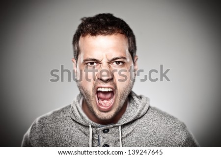 Portrait of a normal man looking furious./ Young man screaming over grey background.