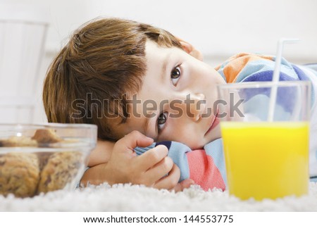 Little boy with cookies and orange juice stretching on carpet./ Closeup of child with breakfast in home.