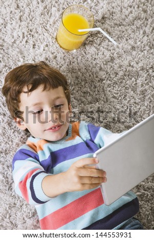 Little boy using a pad./ Child playing with digital tablet stretched on a carpet