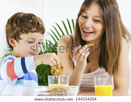 Little boy eating cookies and drinking orange juice with her mum./ Mother and son having breakfast.