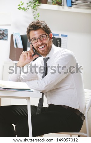 Young businessman talking on smartphone in office. Businessman with rimmed glasses working.