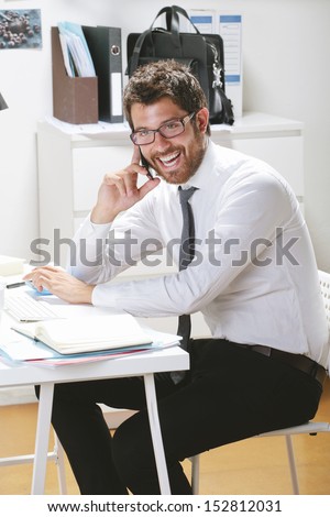 Young businessman talking on smart phone in office. Businessman with rimmed glasses working.
