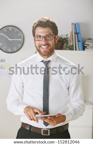 Young businessman looking a camera with digital tablet. Businessman with rimmed glasses in office.