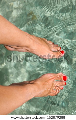 Close up of feet with red nail on sea background. Beauty of red nails of young woman.