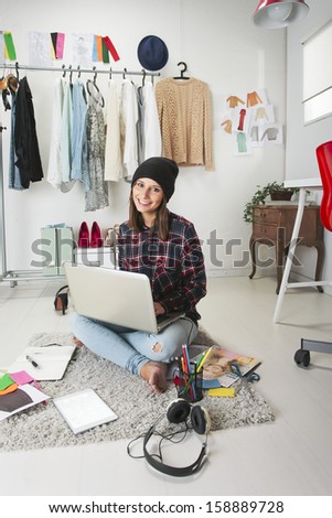 Young creative woman sitting in the floor with laptop./ Casual blogger woman working in her fashion office.