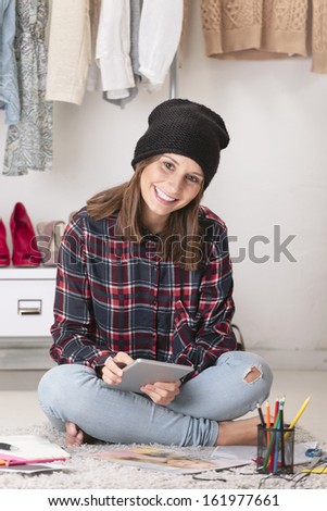 Smiling creative woman sitting in the floor./  Casual blogger working with digital tablet in fashion office.