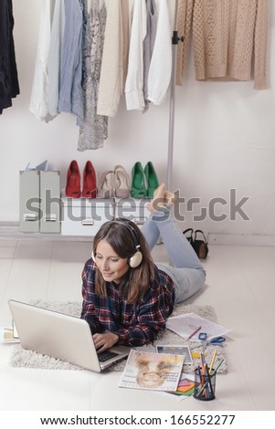 Young creative woman stretched in the floor and listening music./ Casual blogger woman working with laptop in her fashion office.