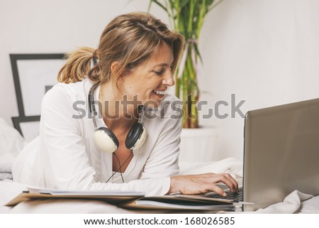 Smiling mature woman typing on computer in the bed./ Happy mature businesswoman working with laptop at home.