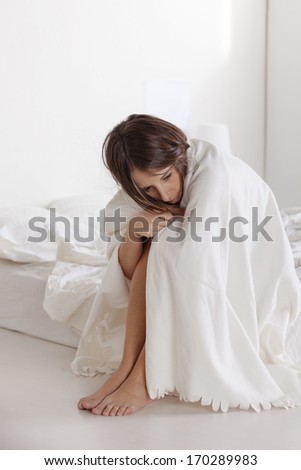 The white bedroom./ Thoughtful young woman sitting on white bed.