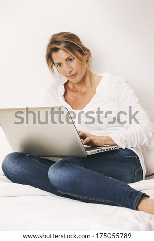 Mature woman typing on computer in the bed.