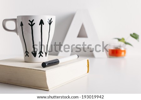 Hipster cup of coffee over a book./ White coffee mug with arrows and diy decoration.
