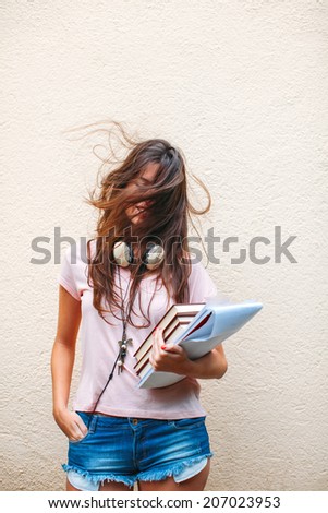 Beautiful woman with headphones subject books and documents./ Portrait of a young student woman with flying hair