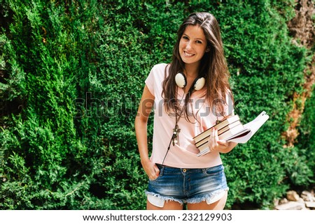 Young beautiful female standing outside with books and documents / Young student woman smiling on home garden.