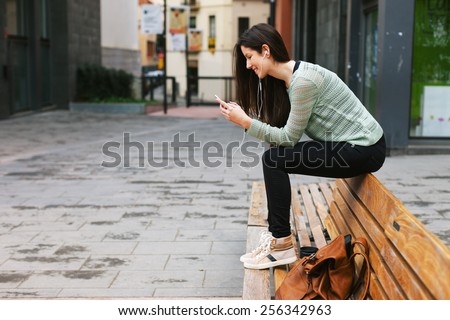 Young woman sitting on a bench in the city./ Young beautiful woman listening to music with phone in outdoors.