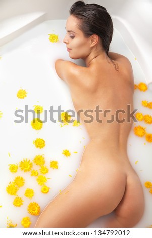 Attractive naked girl enjoys a bath with milk and yellow flowers. Spa body care.