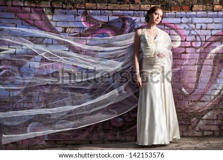 Portrait of beautiful bride standing near colorful wall with flying veil