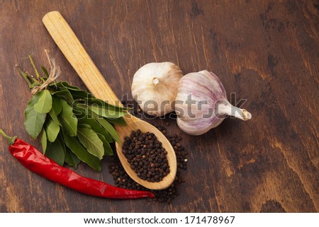 pepper in wooden spoon with garlic, bay leaves and chili pepper. Spices