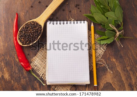 Red chili pepper, garlic, bay leaf, spices in spoons, old notebook on oak wood texture background. Spices