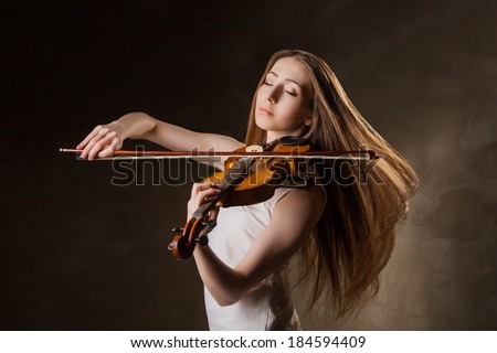 Beautiful young woman playing violin over black background