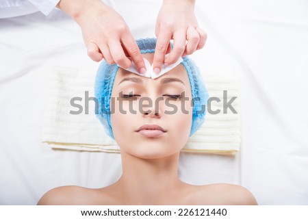 Skin care - woman cleaning face by beautician over white background