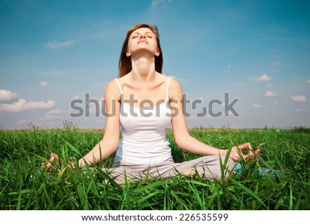 Young girl doing yoga lotus pose in the park over blue sky