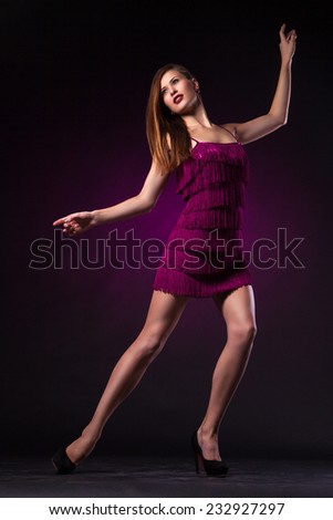 Beautiful sexy young woman in purple dress dancing on dark purple background in studio - series of photos
