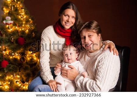 Closeup portrait of cute cheerful family near Christmas tree at home, happy parents with baby celebrate New Year holiday, love concept