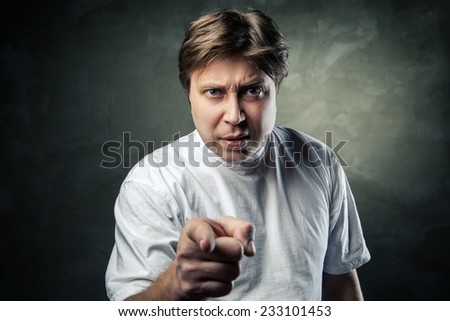 Portrait of angry young man pointing at you over gray background