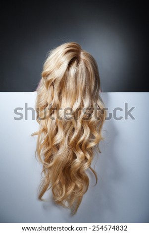 pretty blond model hiding behind a big blank sheet of paper only her hair shown.