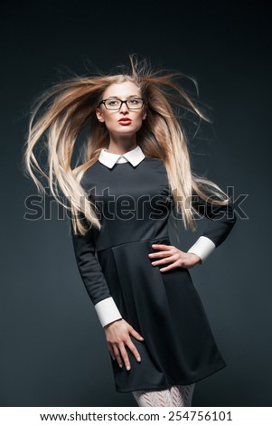 Closeup portrait of blonde young beautiful posing woman wearing eyeglasses and black dress with white collar. Her long hair flurttering in wind