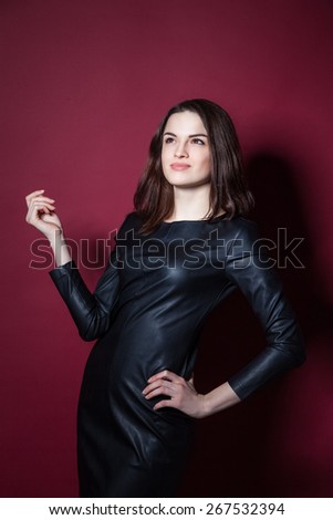 Young beautiful model posing in leather dress on red background