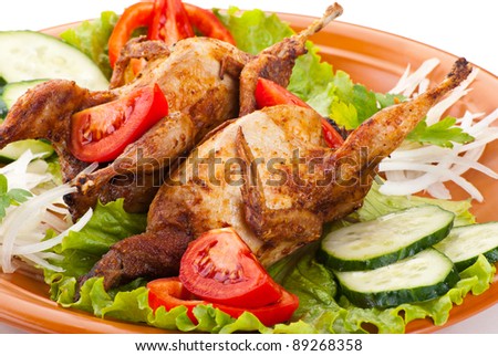 Two fresh grilled whole quail with cucumber, raw tomatoes and onion on plate with leaf lettuce isolated over white background