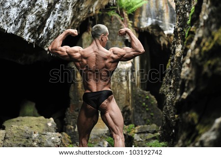 Bodybuilder posing in a cave - posterior back muscles