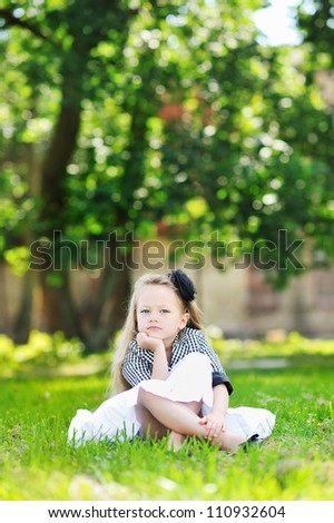 Portrait of serious child resting her chin on hand, while sitting in a park and looking at you. Lots of copyspace