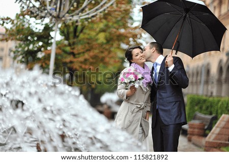 Young happy bride and groom kissing by the rain