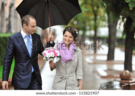 Young happy bride and groom walking by the rain
