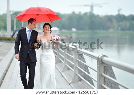 Wedding couple waking by the rain under umbrella