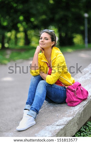 Beautiful girl sit in a park with hand on chin
