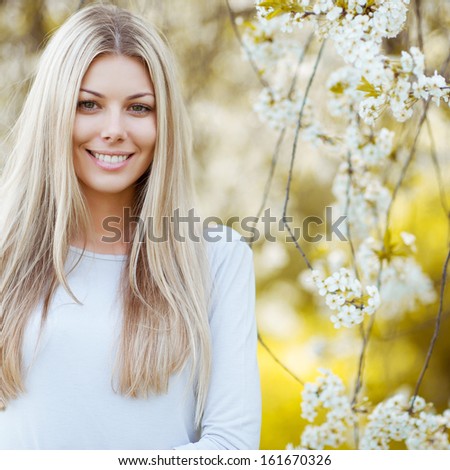 Beautiful young blonde woman standing near the apple tree