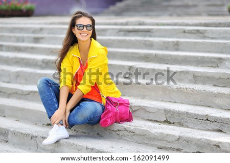 Stylish beautiful girl sitting on a stairs in colorful clothes wearing sunglasses
