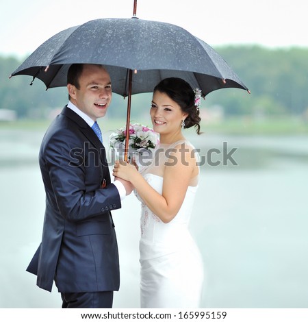 Happy bride and groom in a rainy wedding day hiding from rain