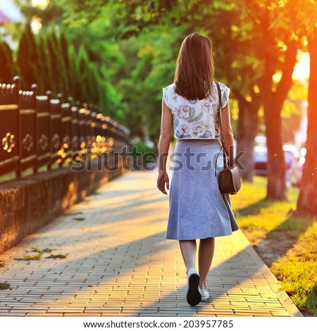 Girl walking away through green alley at the sunset