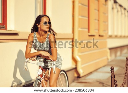 Beautiful young brunette woman sitting on a bike in old town