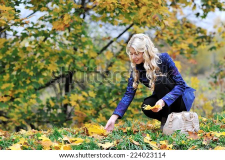 Beautiful elegant woman collects leaves in a park in autumn