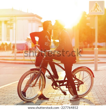 Kissing romantic couple in love Sunset Boy and girl standing near a vintage bike in urban scene Kissing romantic couple in love Sunset Boy and girl standing near a vintage bike in urban scene