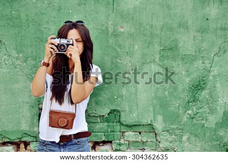 Portrait of stylish young brunette woman in casual clothes with old camera wearing sunglasses