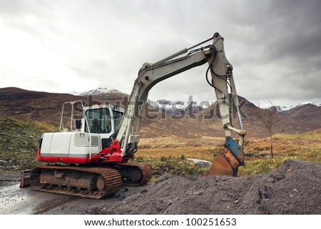 Red and Grey colored earth mover with snow capped mountain landscape scenery in the highlands of Scotland