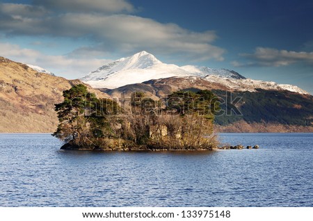 The snow covered top of Ben Lomond  peaking above an island of trees in the waters Loch Lomond