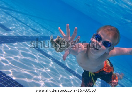 Boy reaching dollar bill, swimming pool underwater shot